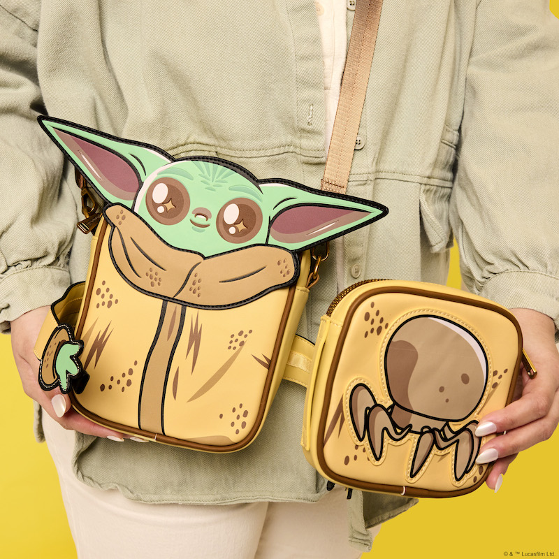 Woman standing against a yellow background holding the Limited Edition Loungefly The Mandalorian Grogu Crossbuddies bag, showing how Grogu's arms open and showing the reverse side of the coin pouch, featuring a crab-like creature.